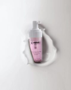 Pink foaming cleanser bottle with pump and liquid splash on white background.