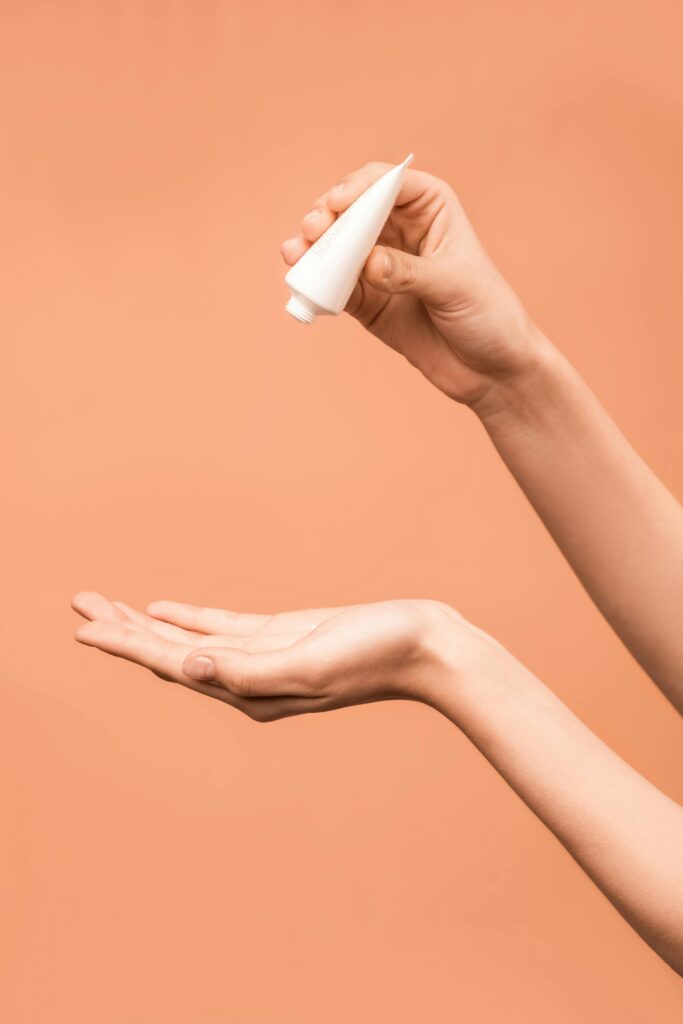 Close-up of hands applying lotion from a tube against a peach background.